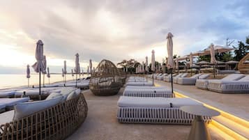 A beachside lounge area with sun loungers, umbrellas, and a unique spherical seating structure.