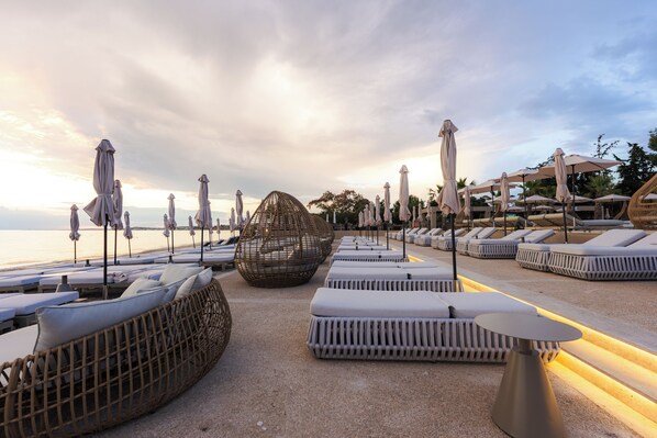 Un espace de détente aménagé au bord de la plage, avec des chaises longues, des parasols et une structure de sièges sphérique originale.