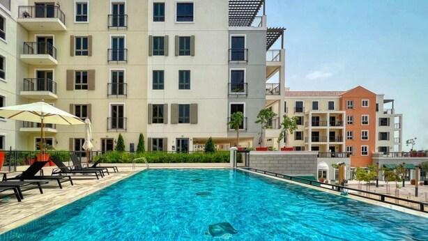 Une piscine entourée de bâtiments à plusieurs étages dotés de balcons, avec des chaises longues et des parasols à proximité.