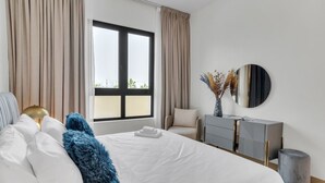 Une chambre d’hôtel moderne avec un grand lit, une table de chevet, une commode et une fenêtre avec des rideaux.