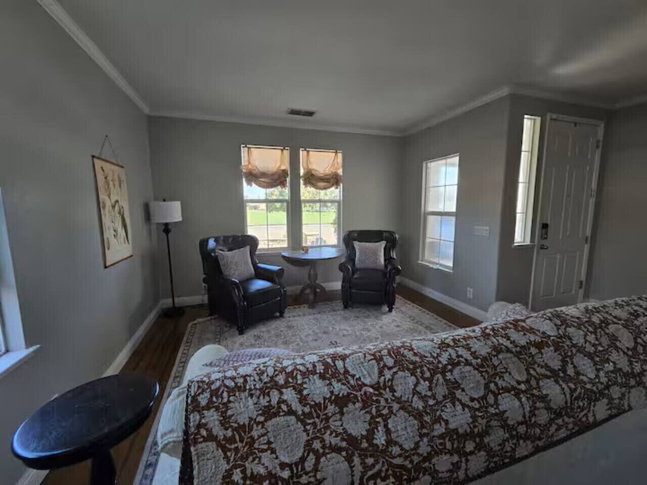 Une chambre à coucher avec deux fauteuils, un lit, une petite table et une fenêtre avec des rideaux.