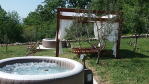 Een hottub in een tuin met een pergola en lounge stoelen.
