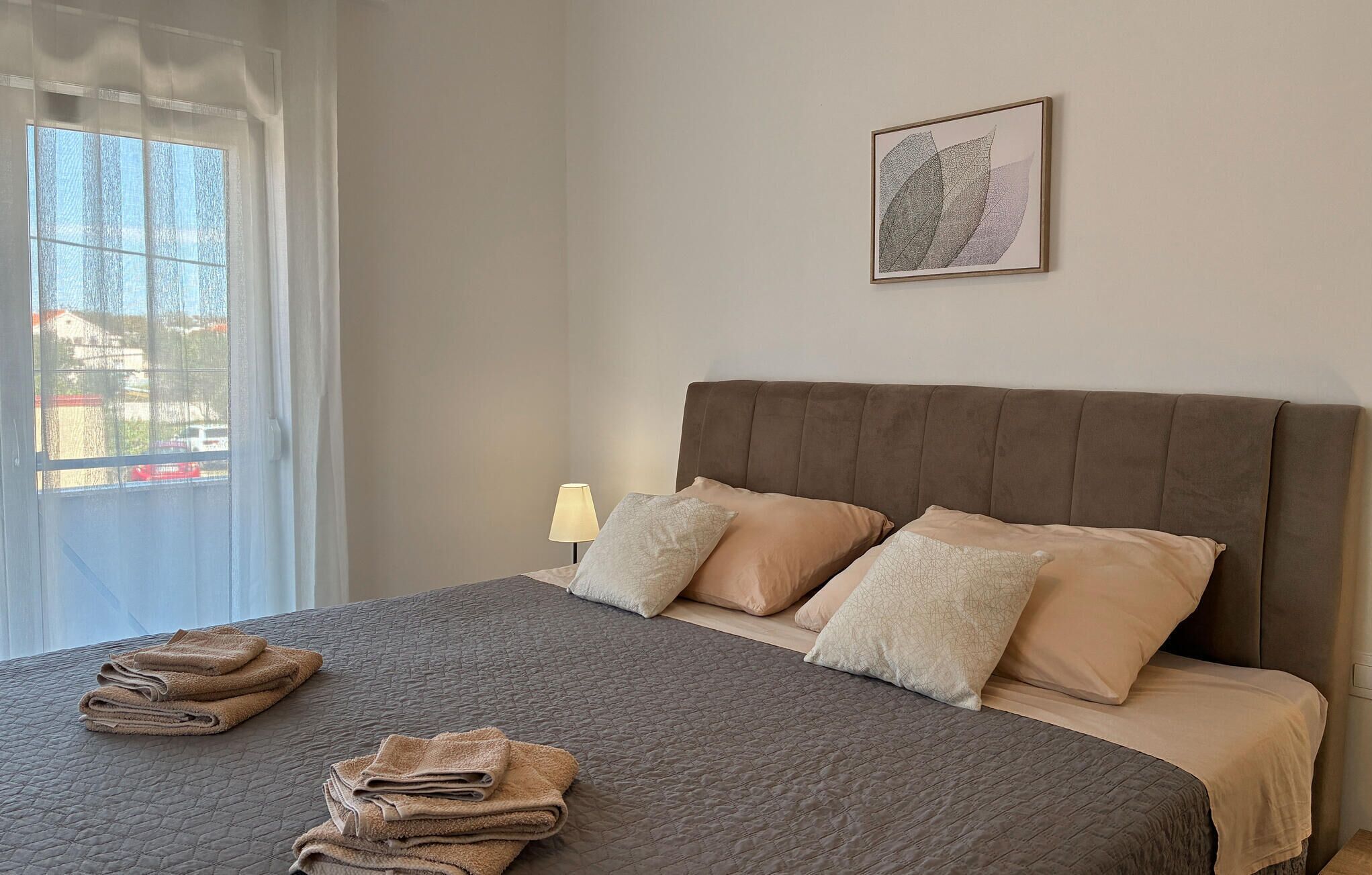 A bedroom with a bed, pillows, a lamp, and a window with curtains.