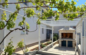 A courtyard with a stone-built outdoor oven, a pergola with climbing vines, and a white building in the background. - Beautiful apartment in Vir with WiFi (Vir)