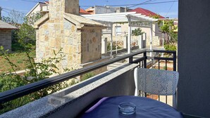 Ein Balkon mit einer Steinsäule, einem weißen Stuhl und einem Tisch mit einem Glas darauf.