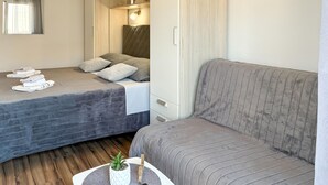 Ein Schlafzimmer mit einem Bett, einem Sofa, einem kleinen Tisch mit Pflanze und einem Fenster mit Vorhängen.