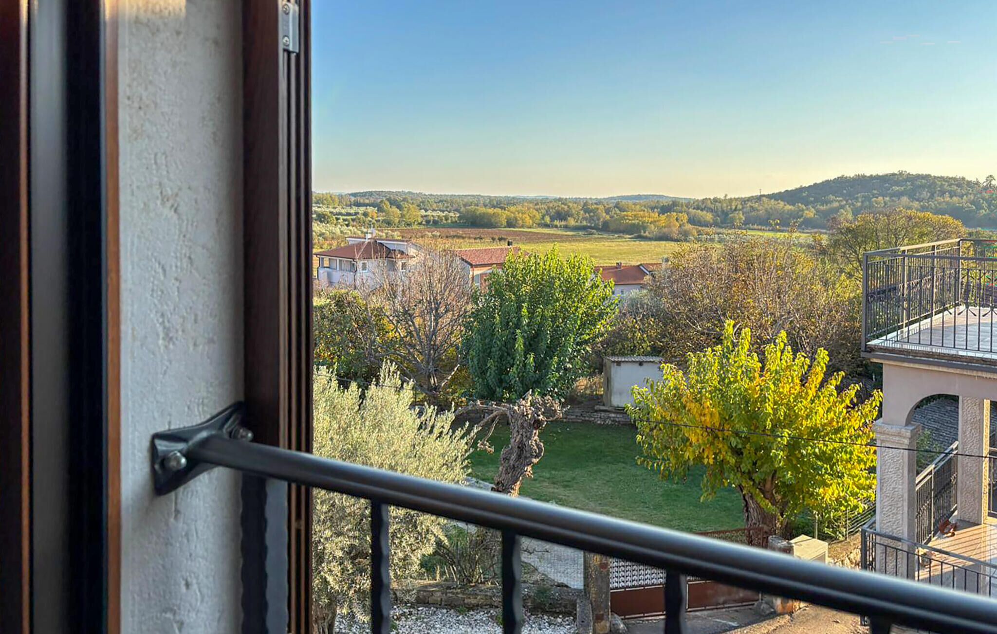 A balcony with a view of a rural landscape, including fields, trees, and distant hills.