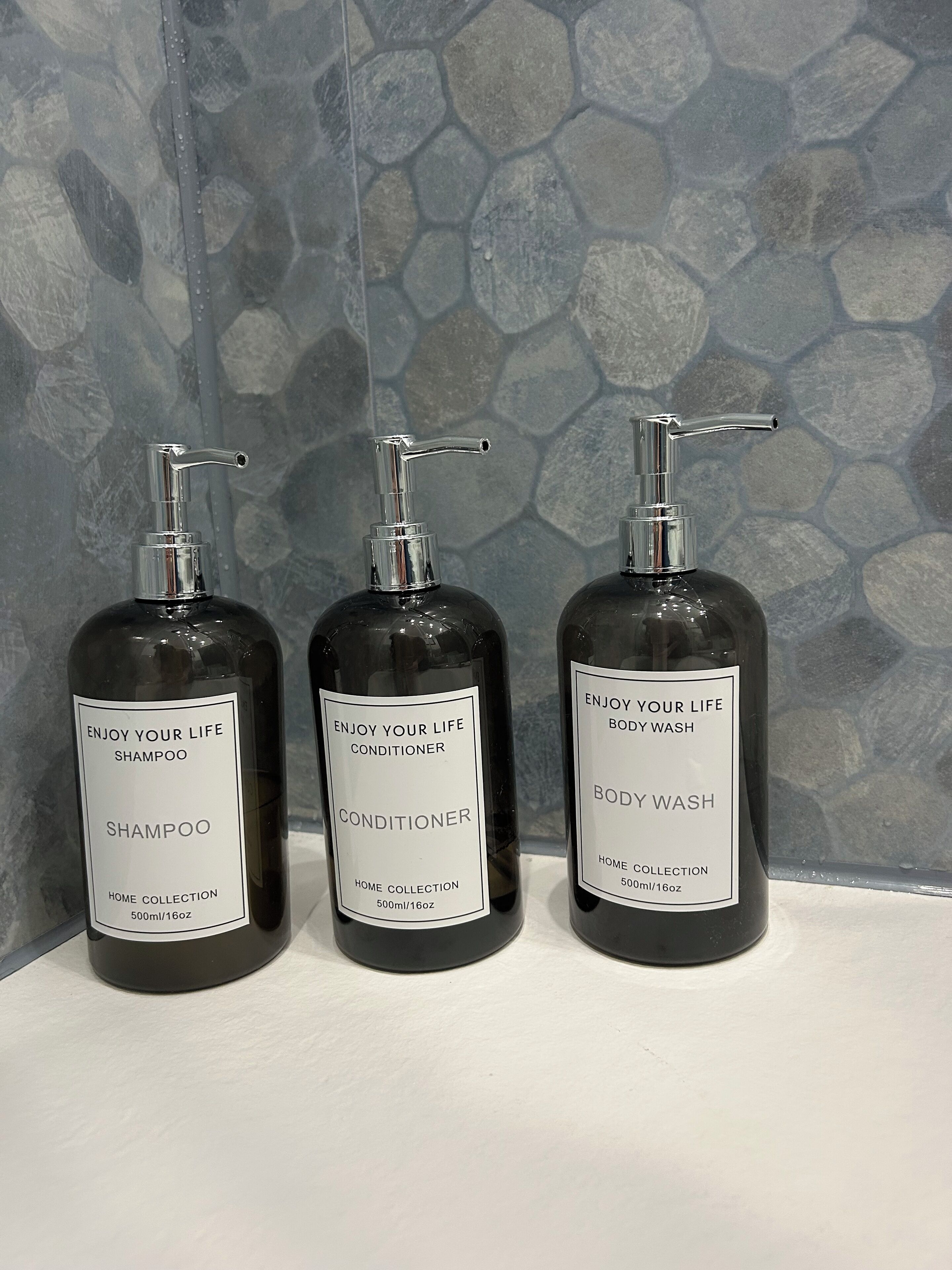 Three bottles of personal care products on a shelf against a stone wall.