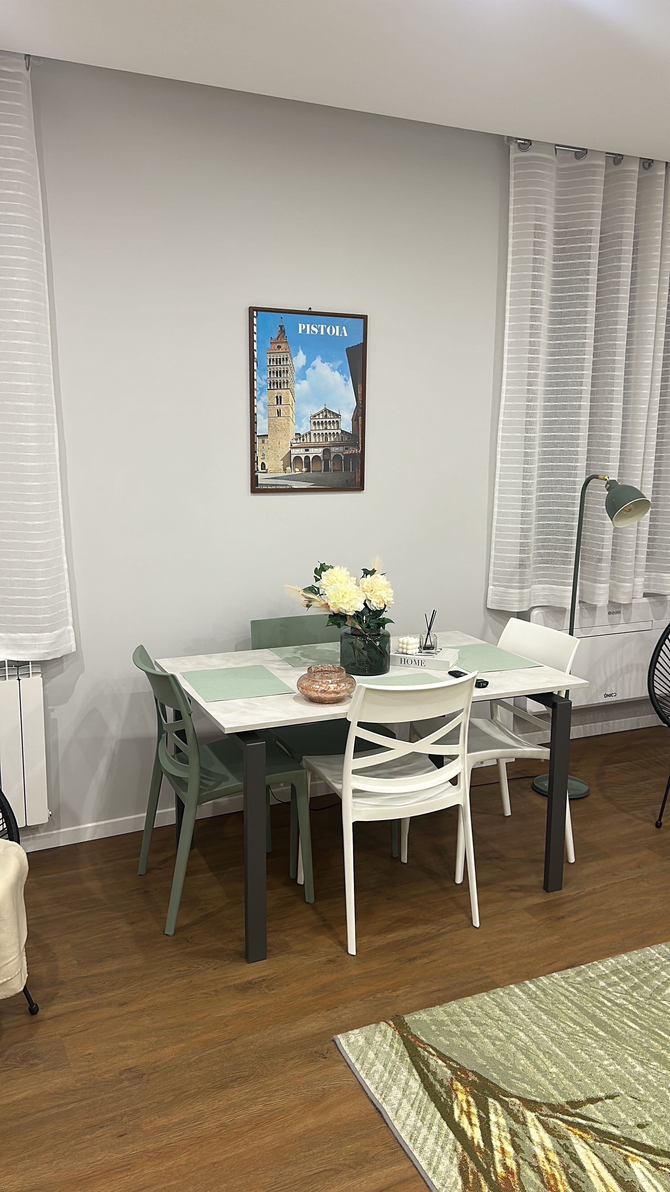 Ein Essbereich mit einem Tisch für zwei Personen, einem gerahmten Bild mit der Aufschrift 'PISTOLA' und einer Lampe auf der rechten Seite.