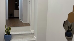 Een wenteltrap met witte muren en marmeren treden die naar een kamer leiden. Er staan potplanten op de treden en aan de muur.