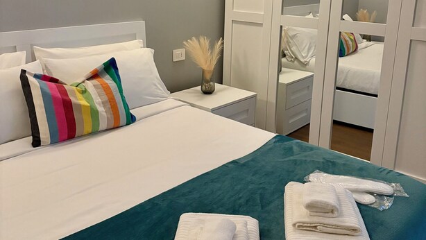Een hotelkamer met een bed, nachtkastje, spiegel en een blauwgroene spreidekker.