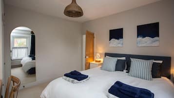 A bedroom with a large bed, a bedside table with a lamp, a mirror, and two paintings on the wall.