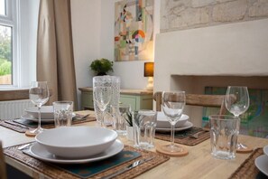 A dining table set with plates, glasses, and cutlery, with a view of a window and a painting on the wall. - Charming Family Cottage in Bath w/Parking (Bath)