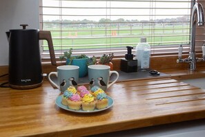 A kitchen area with a coffee maker, mugs, a plate of cupcakes, a window with a view of a field, and a faucet. - Charming Family Cottage in Bath w/Parking (Bath)