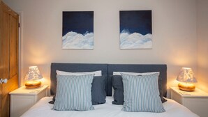 Une chambre à coucher comprenant un lit, deux tables de chevet, deux lampes et deux tableaux représentant des nuages, accrochés au mur.