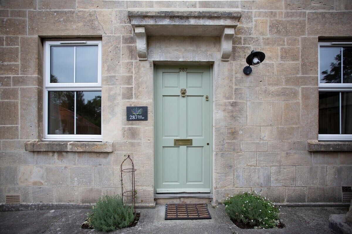 Un bâtiment en pierre avec une porte verte, deux fenêtres et un petit jardin planté.