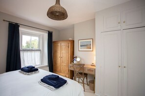 Une chambre à coucher comprenant un lit, un bureau, une chaise, une armoire et une fenêtre avec des rideaux.