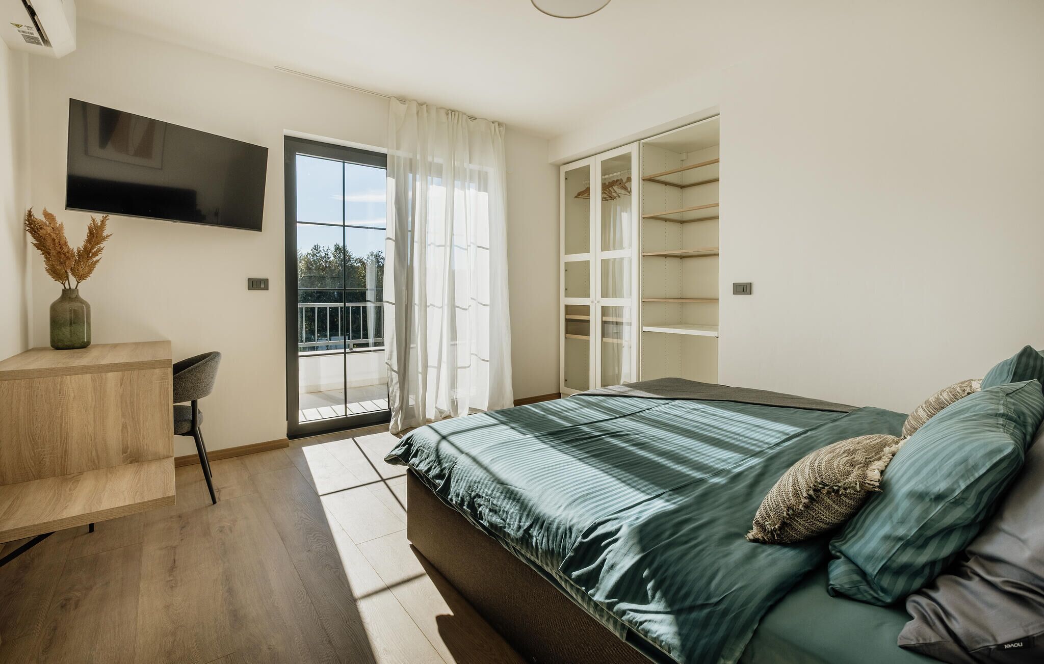 Un dormitorio moderno con una cama grande, televisión montada en la pared, un escritorio y un armario.