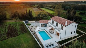 Ein modernes, zweistöckiges Haus mit Swimmingpool, umgeben von üppiger Vegetation und Feldern.