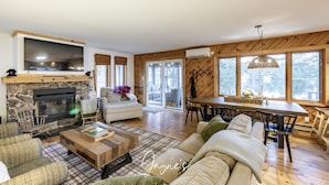 A cozy living room with a stone fireplace, a large TV, and a dining area with a wooden table and chairs. - Dock n Dive (Bala)