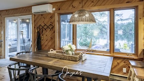 A wooden interior with a dining table, chairs, a hanging light fixture, and large windows offering a view of the outdoors. - Dock n Dive (Bala)