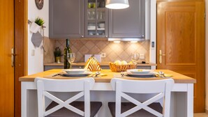 A kitchen with a central island, two white chairs, a hanging light fixture, and a wooden door. - Gorgeous apartment in Silo with outdoor swimming pool (Silo)