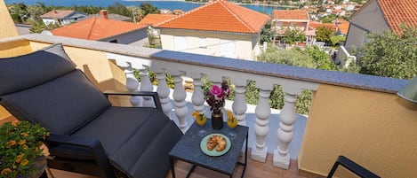 Ein Balkon mit einer Couch, einem kleinen Tisch mit Speisen und Getränken sowie Blick auf eine Küstenstadt.