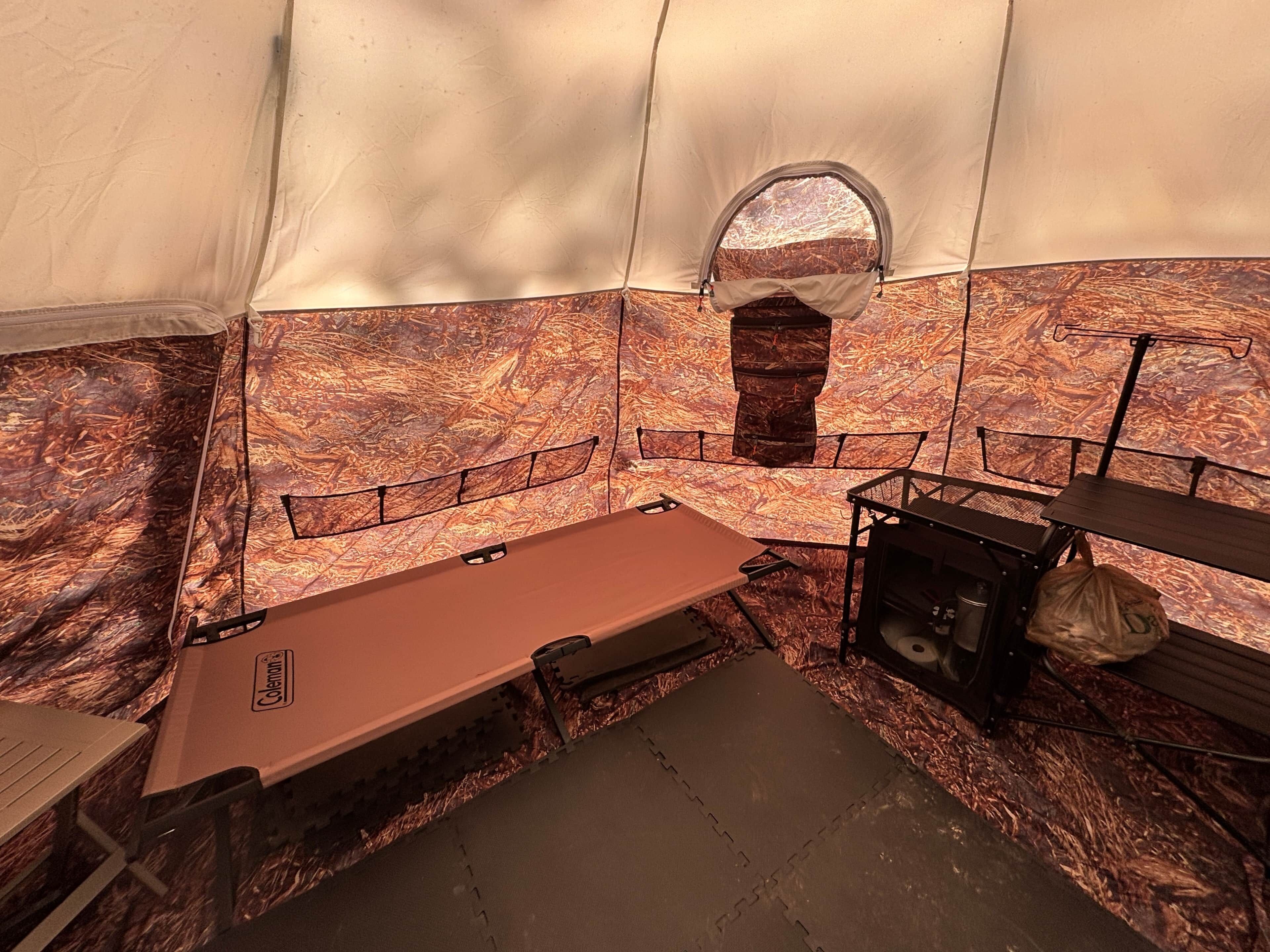 A tent interior with a sleeping area, a small window, and a table with a bag.