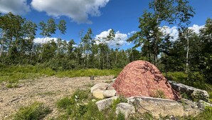 A natural landscape with a large rock formation, trees, and a clear sky.