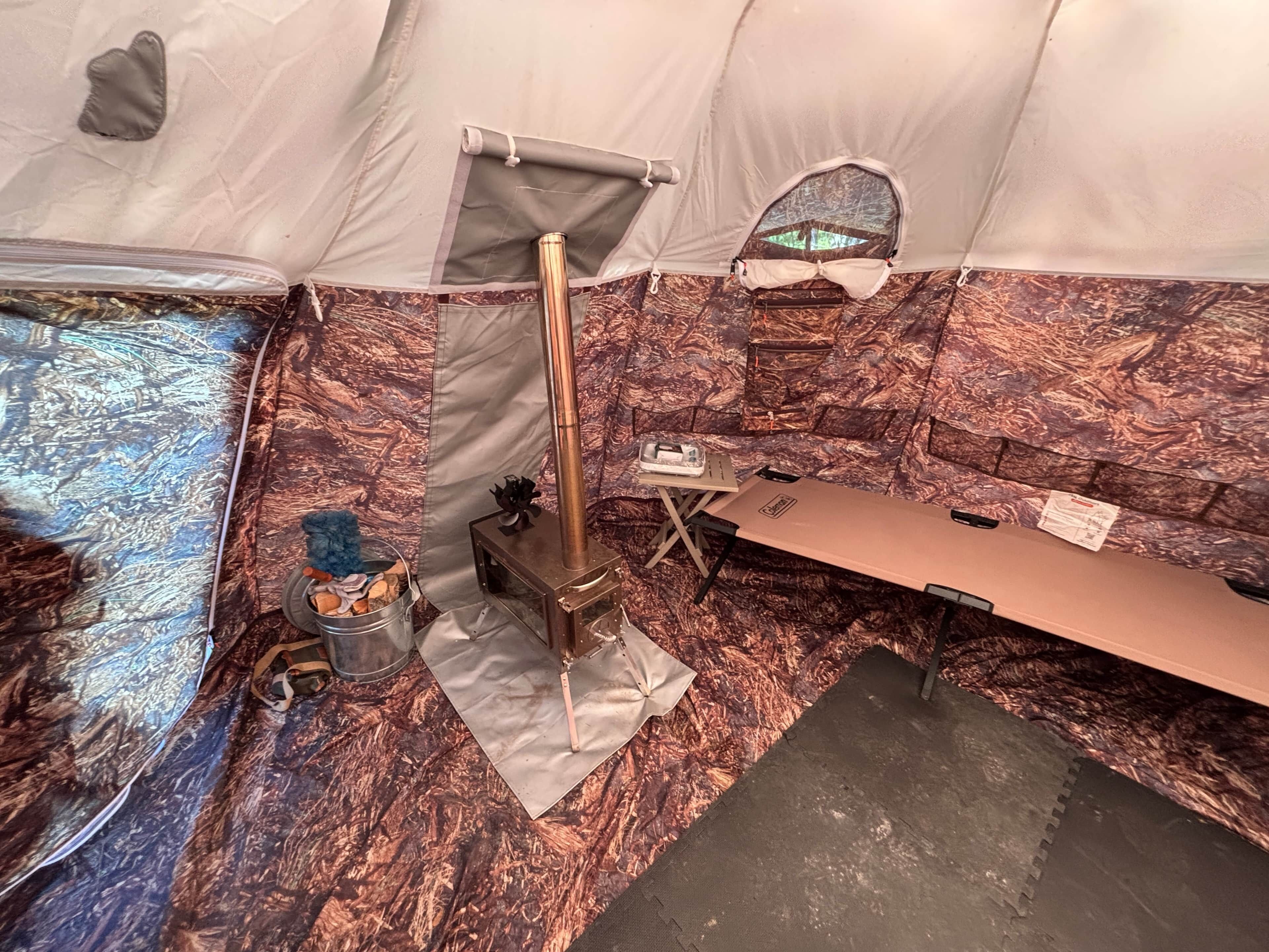 Ein Zeltinnenraum mit einem Campingkocher, einem Tisch und einem Fenster mit Blick auf Bäume.
