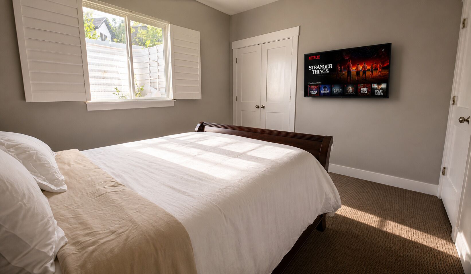 Un dormitorio con cama, televisor montado en la pared y ventana con persianas.