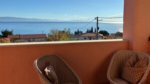 Un balcone con sedie in vimini, vista sul mare e case sullo sfondo.