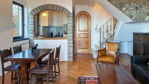 Un'ampia zona giorno con un tavolo e sedie in legno, una poltrona in pelle, un divano e una scala con parete in pietra.