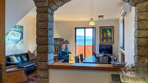 Un soggiorno con arco in pietra, camino, televisione e vista mare attraverso una grande finestra.