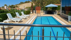 Uma piscina com espreguiçadeiras, uma porta de madeira e um edifício moderno ao fundo.