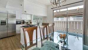 Een moderne keuken met witte kastjes, een roestvrijstalen koelkast, een gasfornuis en een glazen eettafel met stoelen.