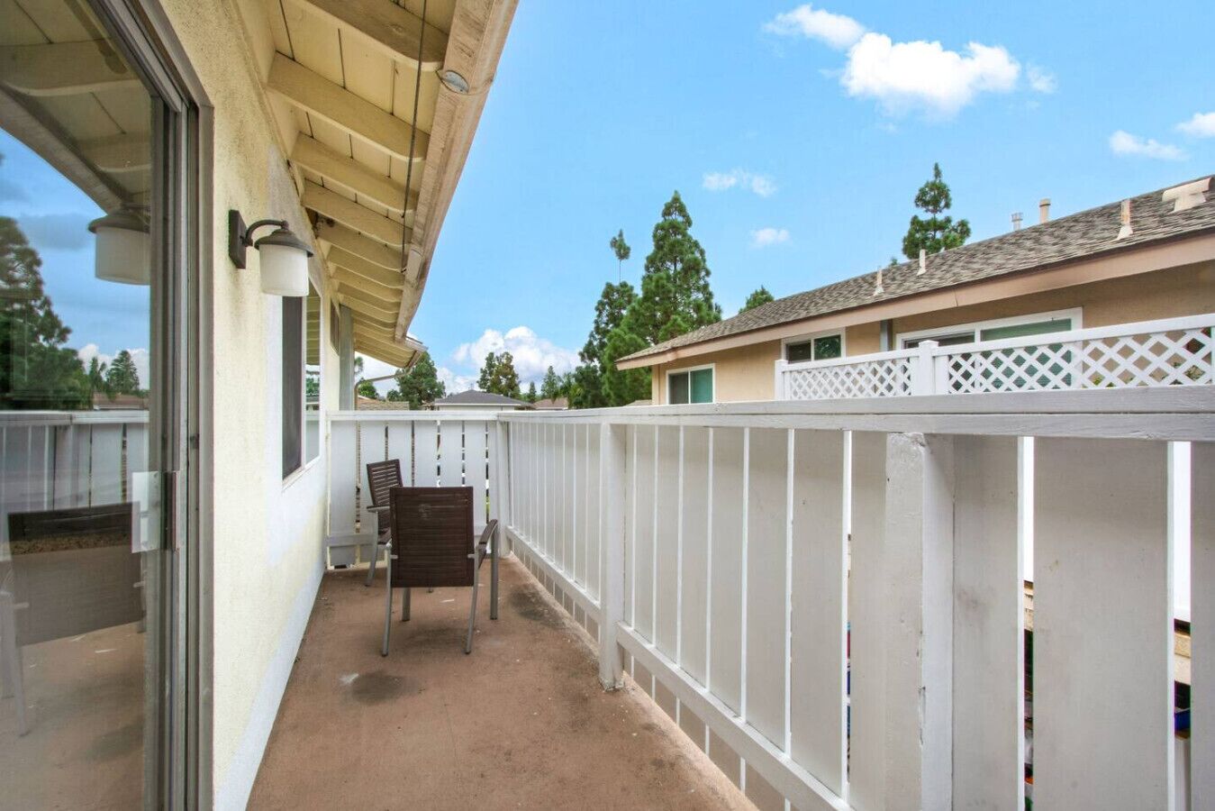 A covered balcony with a white fence, a chair, and a view of neighboring houses.