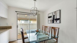 Een eethoek met een glazen tafel en houten stoelen, een moderne kroonluchter en een lijst met een abstract schilderij aan de muur.