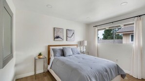 Een slaapkamer met een bed, een nachtkastje met een lamp en twee aan de muur gehangen schilderijen.