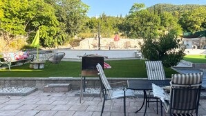 Un patio al aire libre con suelo de piedra, una parrilla y mobiliario exterior, incluyendo sillas y una mesa.