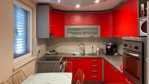 Una cocina compacta con armarios rojos, un lavamanos de acero inoxidable, una cafetera y un horno empotrado.