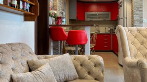 Una sala de estar con un sofá color crema y dos sillas rojas, una cocina con armarios rojos y una pared de piedra.