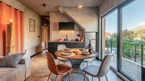 Uma sala de jantar moderna com uma mesa redonda, cadeiras e vista para uma paisagem montanhosa através de grandes janelas.