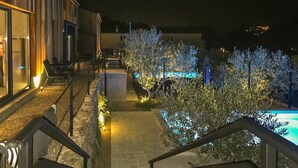 Vista noturna de um pátio de hotel com piscina, área de estar externa e escadaria que leva à entrada.