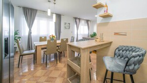 Ein moderner Essbereich mit Holztisch und Stühlen, einem Barhocker und einer Zimmerpflanze.