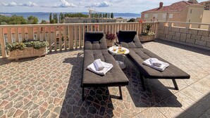 Eine Terrasse mit zwei dunklen Lounge-Stühlen, einem kleinen runden Tisch und einem Blumentopf.