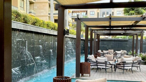 An outdoor lounge area with a pool, cushioned seating, and a pergola providing shade. - spacious apartment w/ pool and garden view (Cairo Governorate)