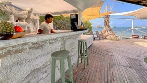 A wooden deck with a bar area, outdoor seating, and a view of the ocean. - El Arca (Isla Tintipán)