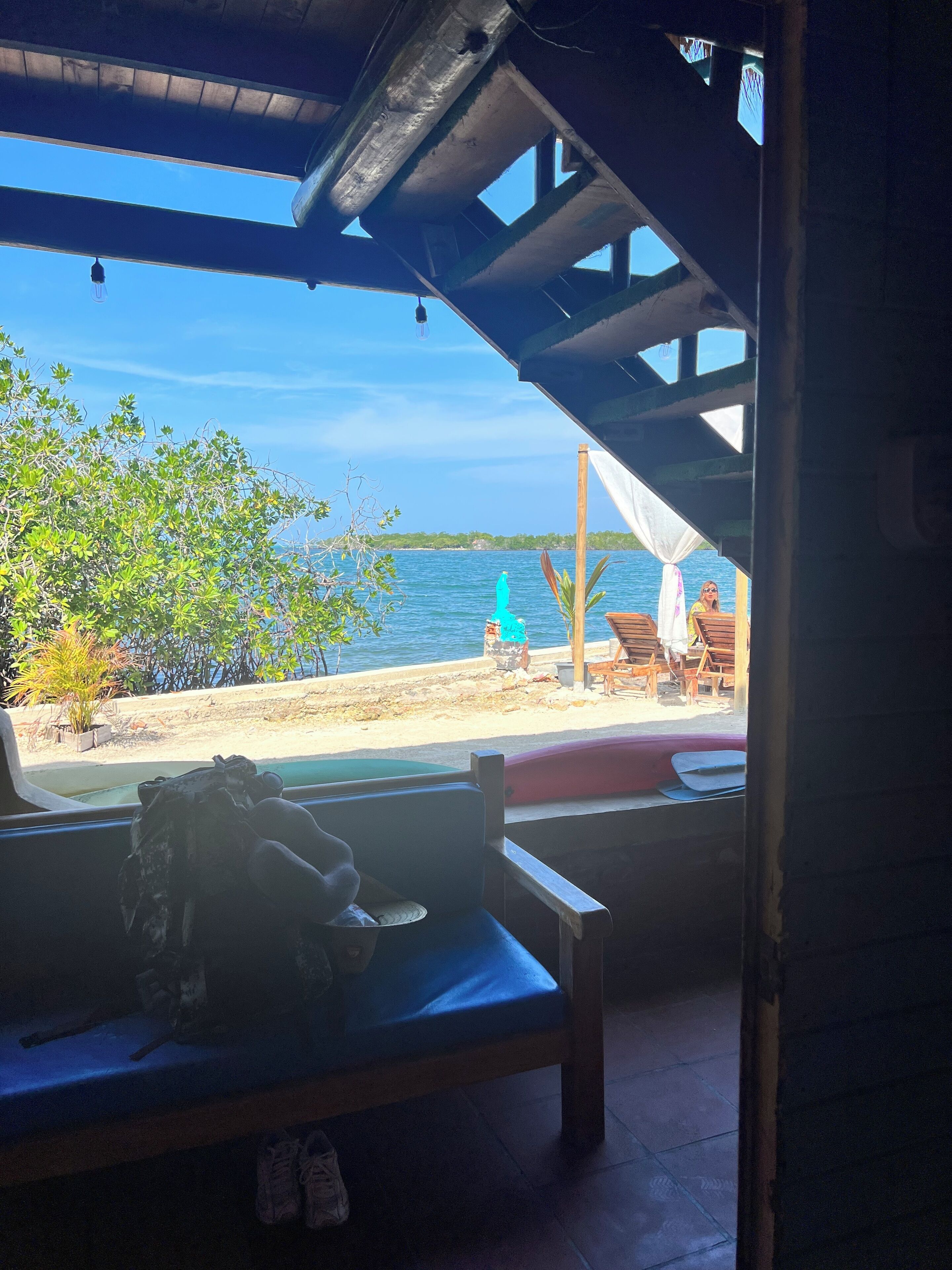 Vista desde una zona cubierta con banco y mesa, con vista al mar y a la playa de arena.