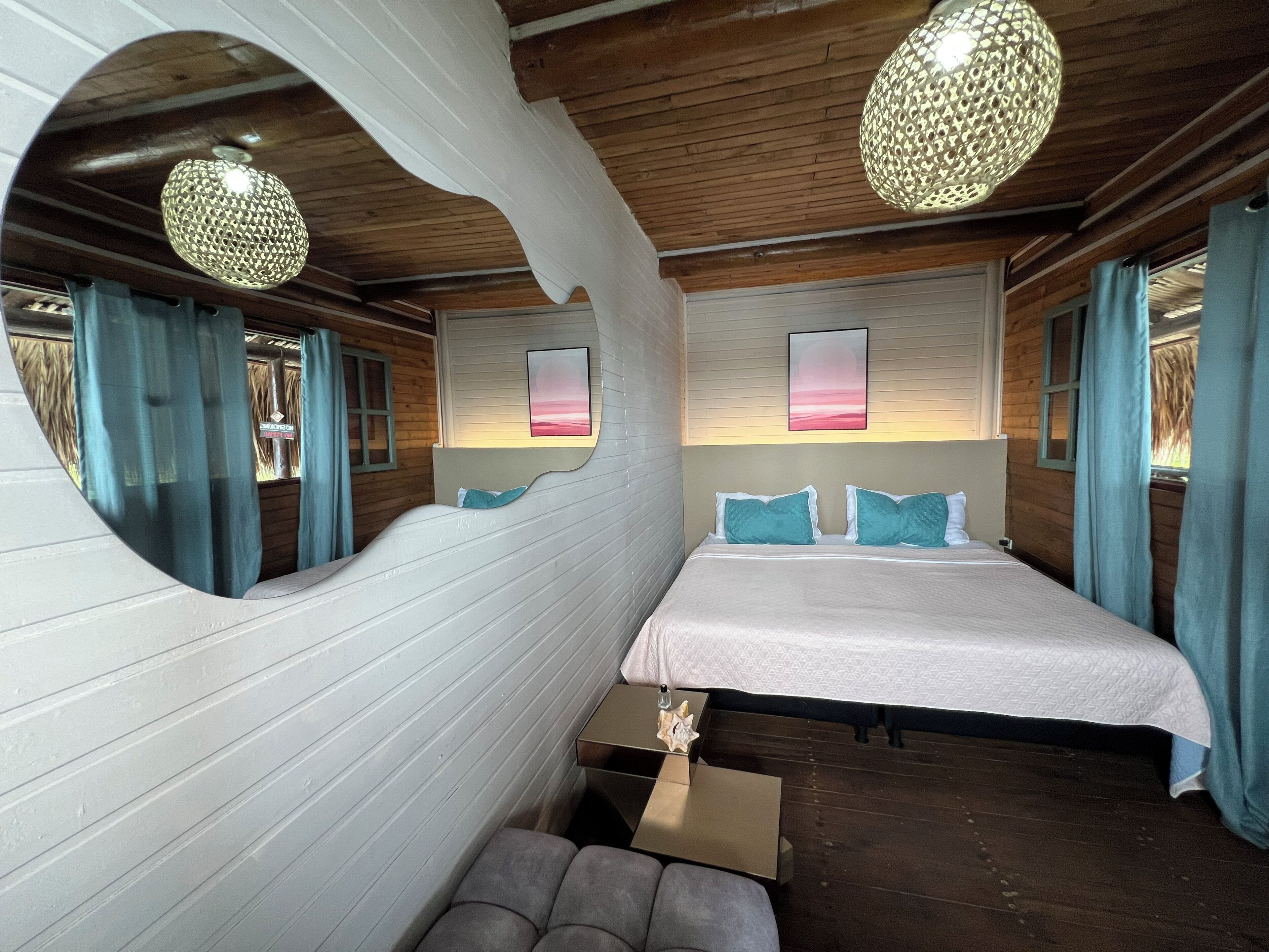 A bedroom with a large bed, two bedside tables, a mirror, and a hanging light fixture.